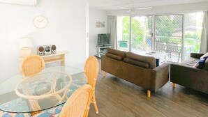 A living room with a glass table, wicker chairs, a brown sofa, and a television.