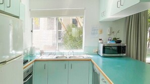 A kitchen with teal cabinets, a microwave, and a window with a view of greenery outside.