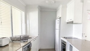 Une cuisine étroite avec des meubles blancs, un lave-vaisselle, un réfrigérateur et une cuisinière.