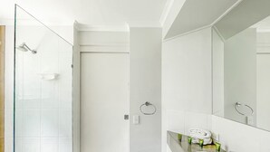 Une salle de bain moderne avec une douche à parois de verre, un lavabo blanc avec un miroir et une petite poubelle.