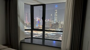 Habitació d'hotel amb una finestra gran que ofereix vistes a un paisatge urbà de nit.
