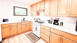 A compact kitchen with wooden cabinets, a gas stove, a sink, and a window with a view of greenery. - Cozy Studio Cottage with Harbor View/Spacious Full Kitchen & Pet Friendly (Bodega Bay)