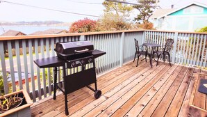 A wooden deck with a grill, two chairs, and a table. - Cozy Studio Cottage with Harbor View/Spacious Full Kitchen & Pet Friendly (Bodega Bay)