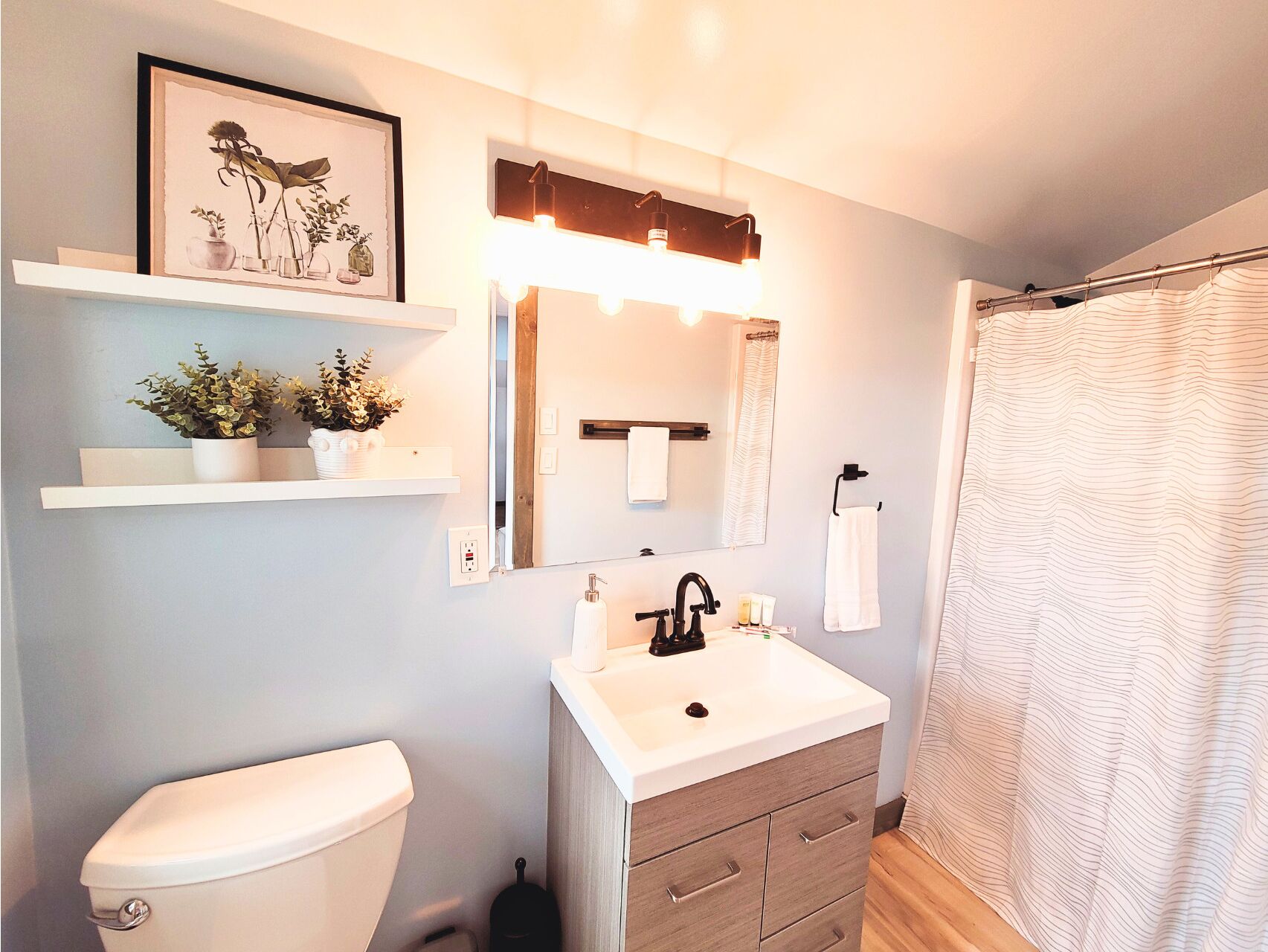 Un baño con inodoro, lavamanos, espejo y cortina de ducha.