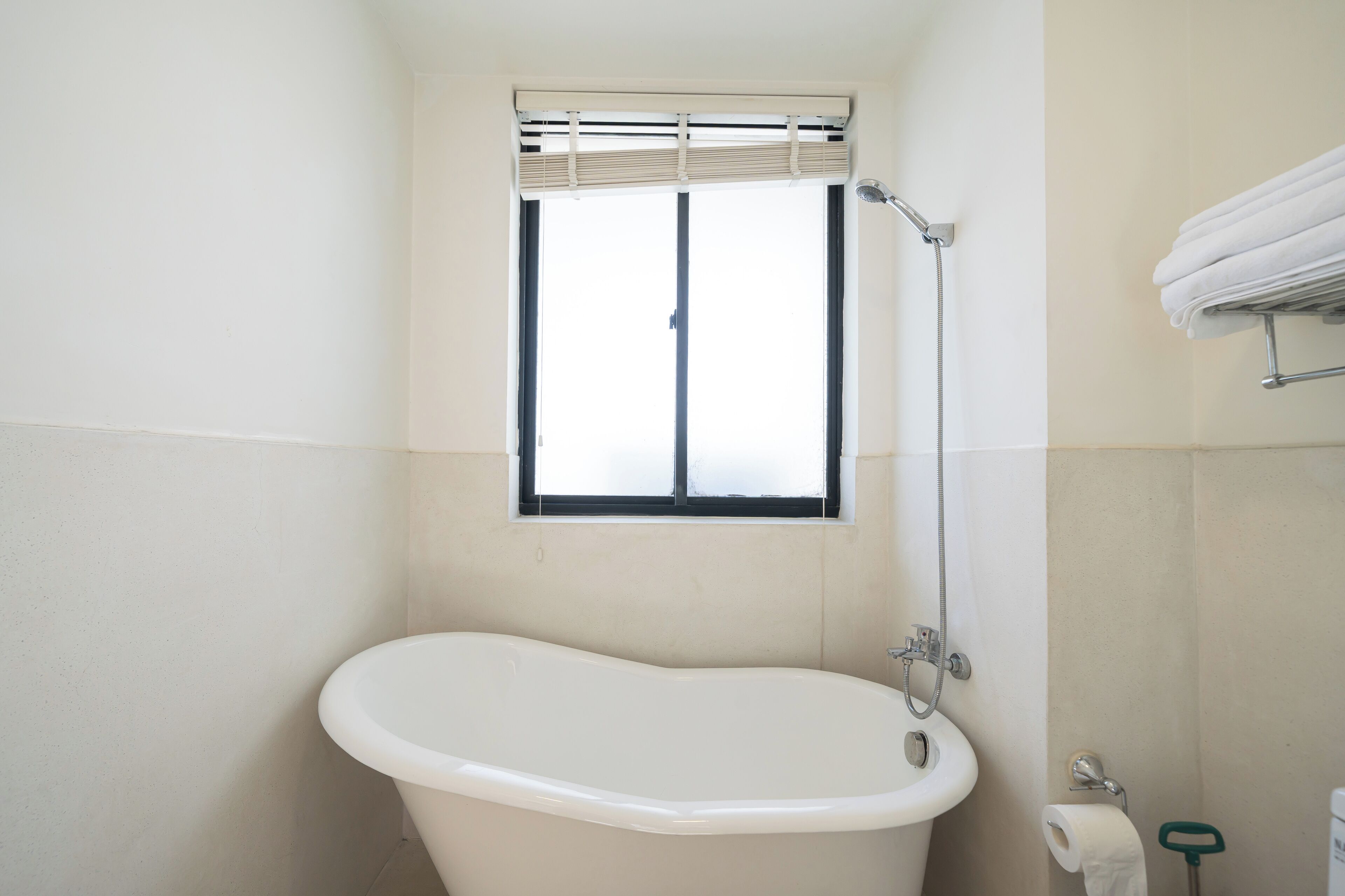 Une salle de bain avec une baignoire sur pieds, une fenêtre avec des stores, un porte-serviettes et des toilettes.