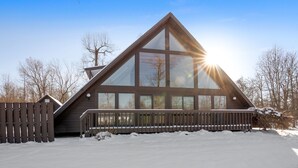 Ett modernt hus med ett stort glasfönster, en träveranda och en snötäckt mark.