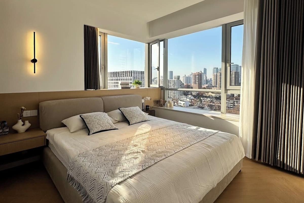 Ein modernes Schlafzimmer mit großem Bett, Blick auf die Stadt und minimalistischer Einrichtung.