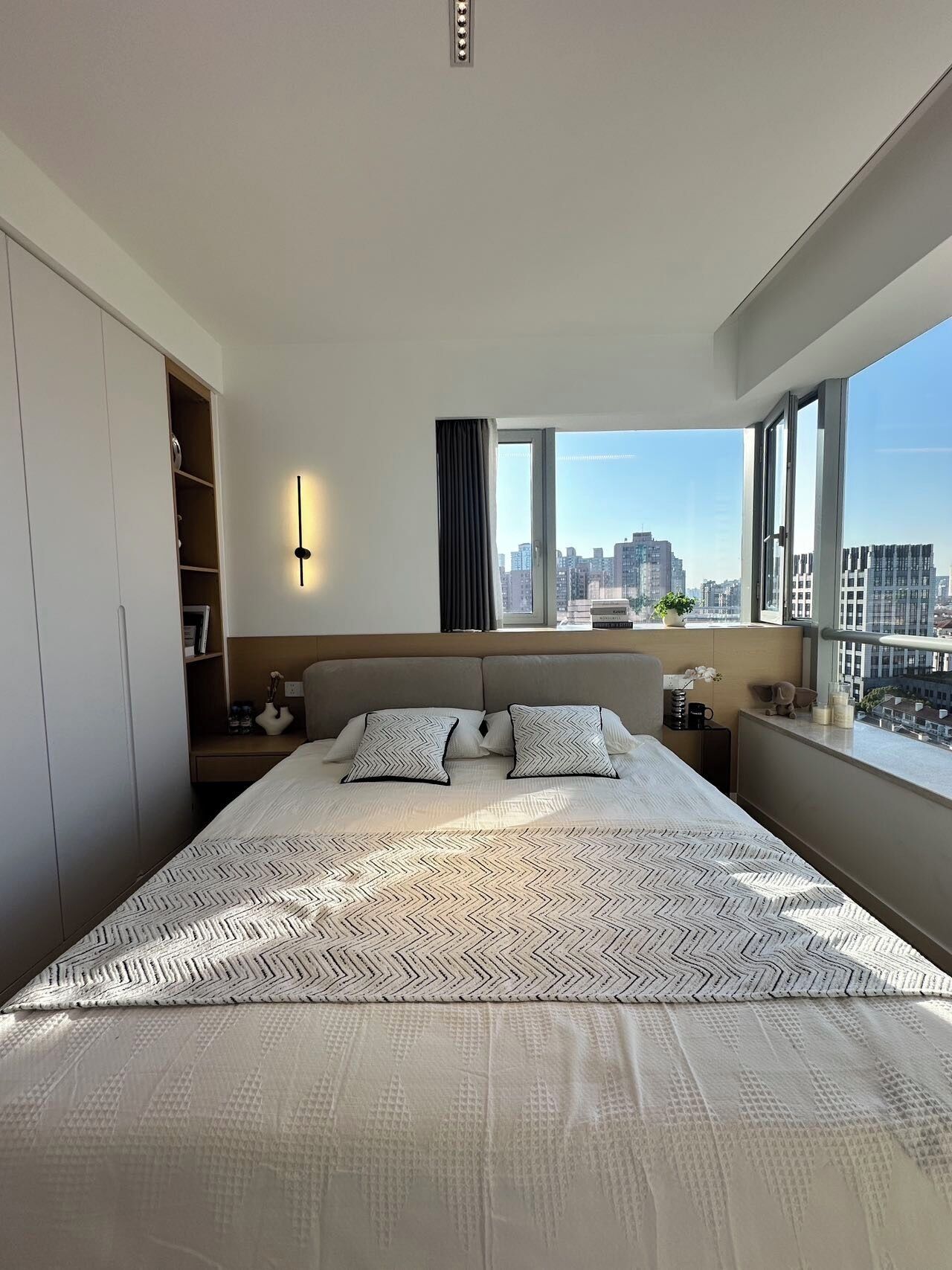 Une chambre moderne avec un grand lit, une vue sur la ville, un placard intégré, des tables de chevet et une table de nuit.