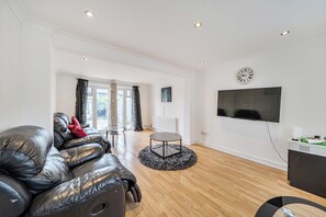 A modern living room with a leather sofa, a round coffee table, and a flat-screen TV mounted on the wall.