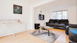 A spacious living room with a white radiator, a black leather sofa, a glass coffee table, and a painting on the wall.