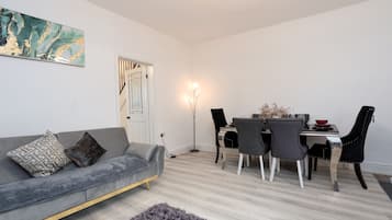 Un salon moderne avec un canapé gris, une table à manger avec des chaises, un lampadaire et un tableau au mur.