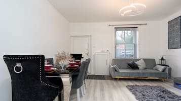 Un salon moderne avec un canapé gris, une table à manger avec des chaises, un vase décoratif et un tapis gris.
