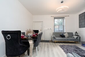 A modern living room with a grey sofa, a dining table with chairs, a decorative vase, and a grey rug. - Cosy Cottage - Sleeps 6, Parking & Pet Friendly! (Nelson)