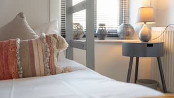 Un lit bien fait, avec des oreillers, une lampe de chevet et des vases décoratifs posés sur le rebord d’une fenêtre.
