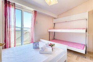 A hotel room with a bunk bed, a large bed, and a window with curtains.