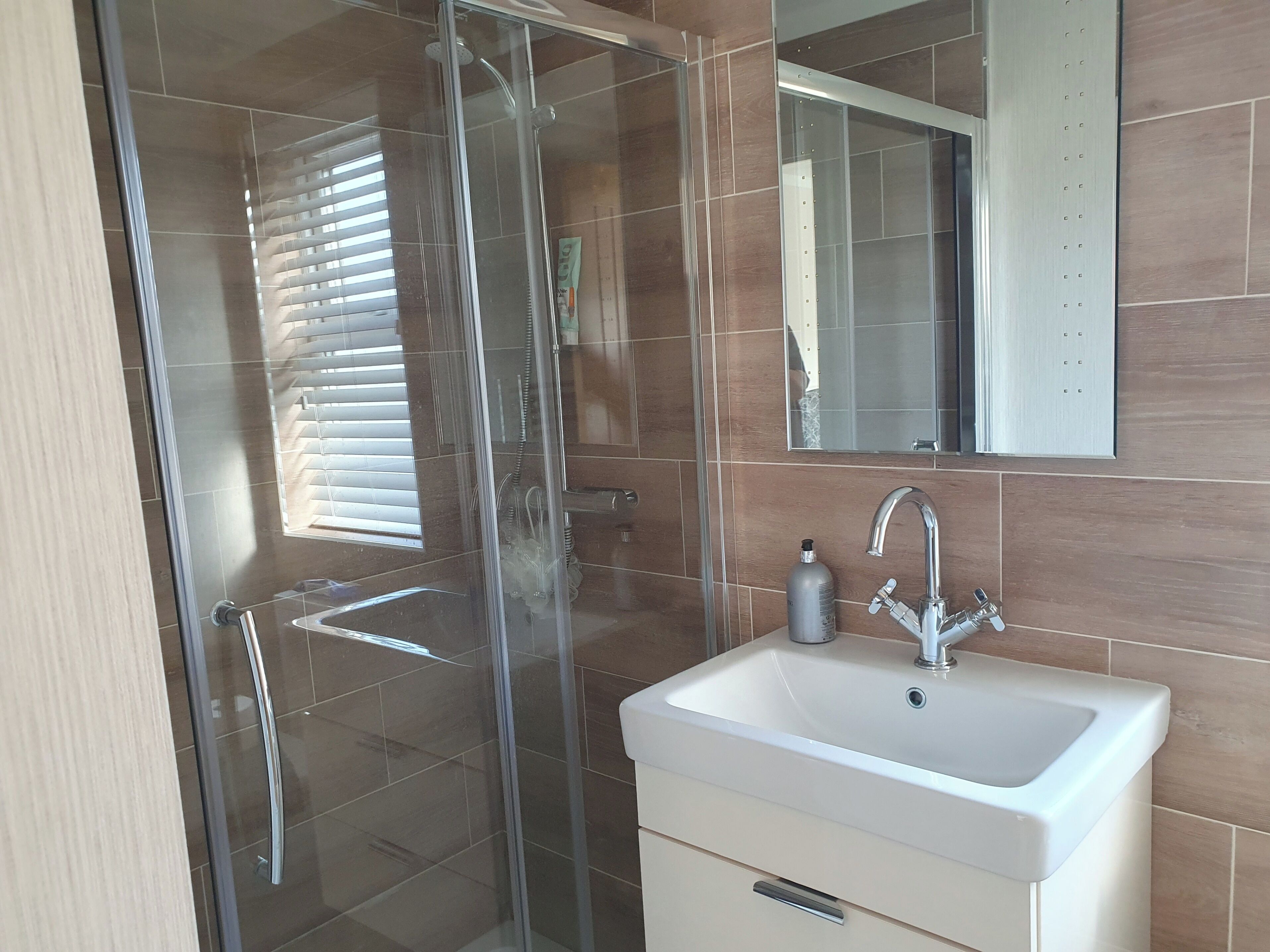 A modern bathroom with a glass-enclosed shower, a white sink, and a mirror above it.