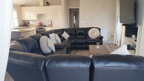 Un salon moderne avec un canapé d’angle en cuir noir, une table basse et un téléviseur à écran plat fixé au mur.