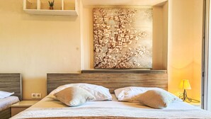 Une chambre d’hôtel avec un grand lit, une tête de lit en bois, une étagère fixée au mur avec une plante en pot, et une grande œuvre d’art florale au-dessus du lit.