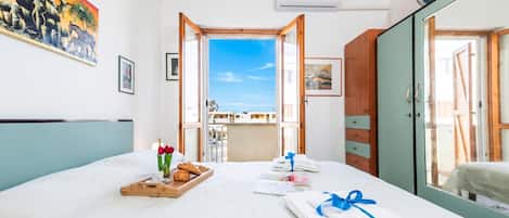A hotel room with a bed, a breakfast tray, towels, a painting, and a view of the outside.