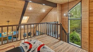 A wooden interior with a sloped ceiling, a staircase, and a large window offering a view of greenery.