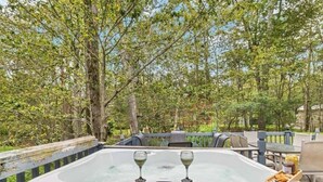 A hot tub with two glasses of wine, surrounded by outdoor furniture and trees.