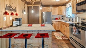 A kitchen with wooden cabinets, a stainless steel refrigerator, a coffee station, and a bar area with stools.