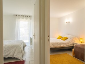 Une chambre avec deux lits, une fenêtre avec un rideau, une table de chevet avec une lampe et un tapis rouge.