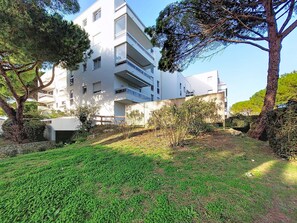 Um edifício moderno de vários andares com varandas, rodeado por vegetação e árvores.