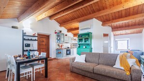 A spacious living area with a wooden ceiling, a dining table set with chairs, a sofa, and a kitchen with cabinets and a stove.