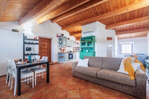 A spacious living area with a wooden ceiling, a dining table set with chairs, a sofa, and a kitchen with cabinets and a stove.