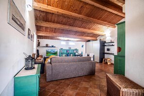 Ein geräumiger Wohnbereich mit hoher Holzbalkendecke, einer Couch, einem Fernseher und einer Küchenzeile mit einem grünen Schrank.