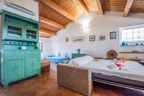 Una habitación con una cama, un armario verde, una silla de mimbre y una ventana con vistas.