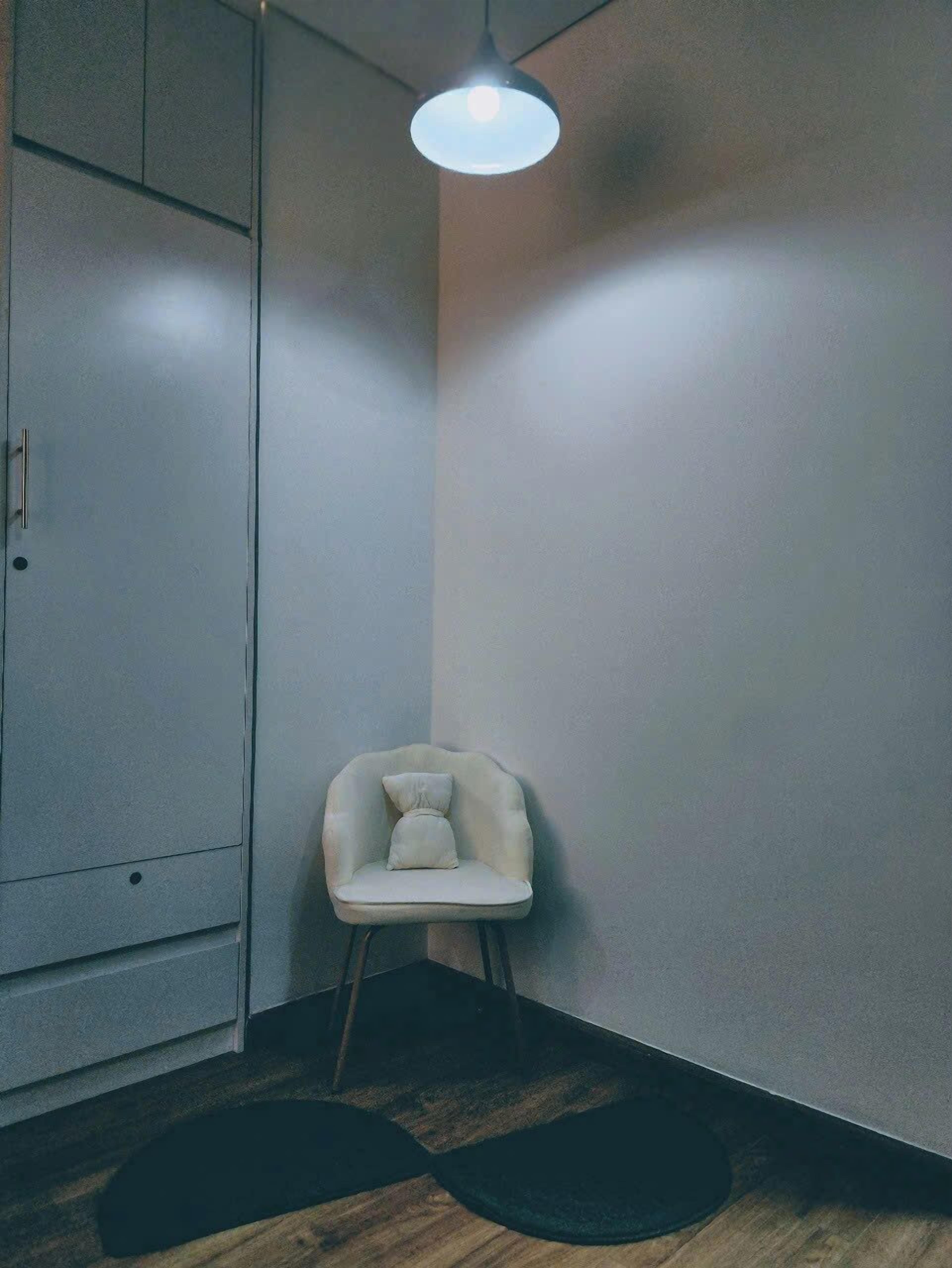 A corner room with a white chair, a hanging light fixture, and a wardrobe.