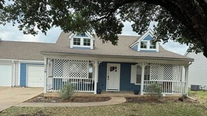 A two-story house with a front porch, a garage, and a tree in the background.