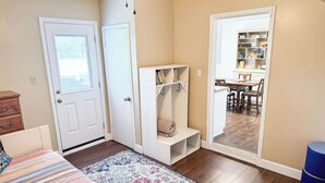 A bedroom with a bed, a wardrobe, a door, a small seating area, and a view into a dining area.