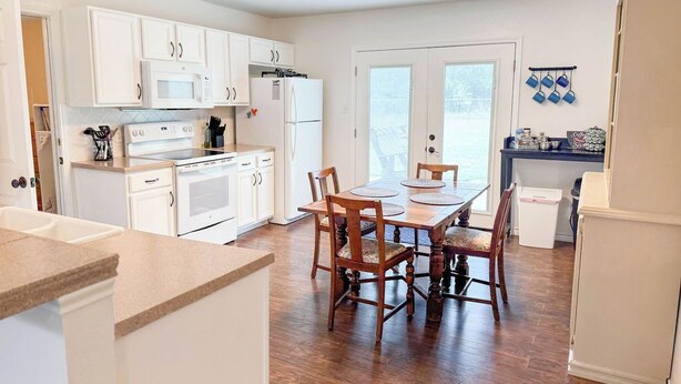 A modern kitchen with white cabinetry, a dining table with chairs, and a refrigerator.