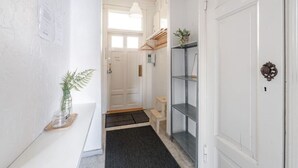 Un pasillo con una puerta blanca, un pequeño estante con una planta, un banco de madera y un felpudo en la entrada.