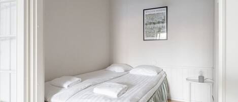 A bedroom with a bed, pillows, a bedside table, and a framed picture on the wall.