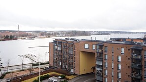 Een meerlaags gebouw met een gele gevel, een parkeerplaats en uitzicht op een waterpartij en verre gebouwen.