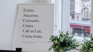 A framed menu listing items like 'Éclairs, Macarons, Croissants, Crêpes, Café au Lait, Crème brûlée' in a café setting with a window view. - Renovated Loft in a Historical Downtown Building (Tampere)