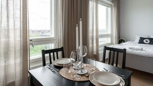Ein ordentlich gedeckter Esstisch mit Kerze, Tellern und Besteck, platziert in einem Zimmer mit Bett und einem Fenster mit Vorhängen.