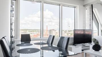 A modern dining area with a glass table, black chairs, and a city view through large windows.