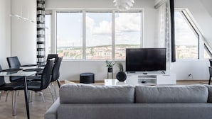 Una sala de estar moderna con un ventanal grande, un televisor de pantalla plana, un comedor con sillas y un sofá.
