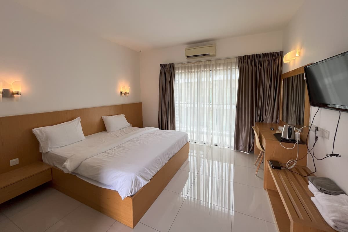 A hotel room with a wooden bed, a desk with a chair, a TV, and a window with curtains.