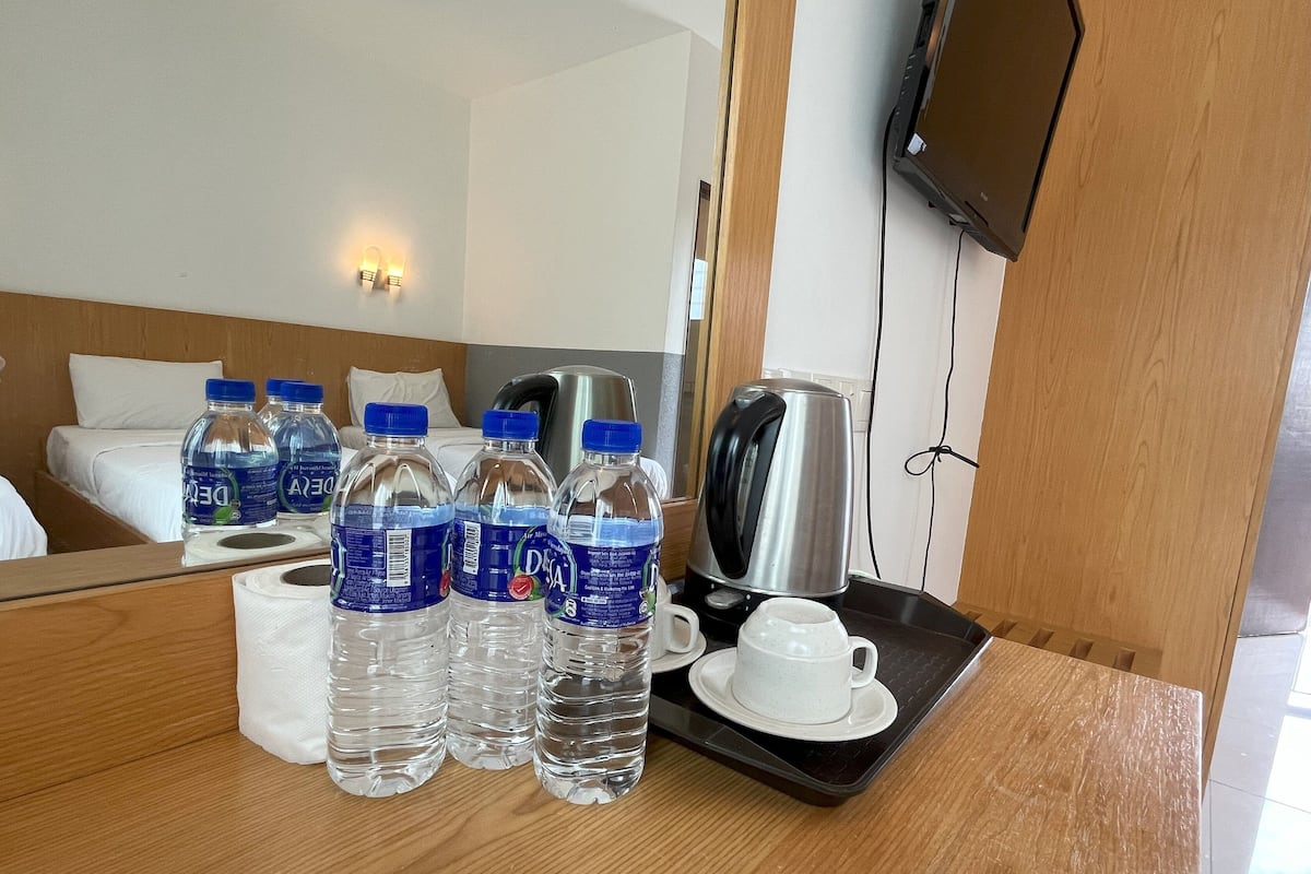 A hotel room with a wooden bed, a bedside table with water bottles, a kettle, and a cup and saucer.
