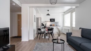 A modern living room with a grey sofa, a TV, and a dining area with a table and chairs.