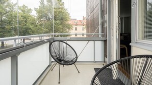 A balcony with a black chair and a smaller chair, overlooking a street with trees and buildings.