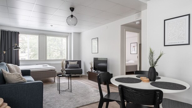 A modern living room with a sofa, a TV, a dining table with chairs, and a large window with curtains.