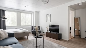 A modern living room with a sofa, a bed, a TV, and a large window.