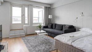 Un dormitorio moderno con un sofá gris, una cama, una pequeña mesa blanca y una lámpara de pie.
